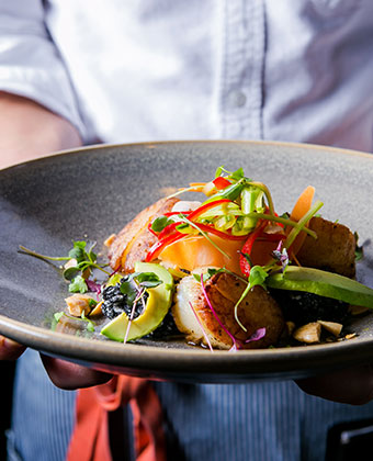 Waiter holding scallops on a bed of fresh greens